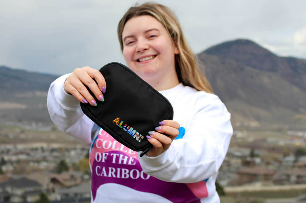 Shae holding out retro alumni fanny pack while wearing retro TRU / Cariboo College sweater